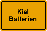 Straßenschild in Orange mit der Aufschrift "Kiel Batterien" in schwarzer Schrift.