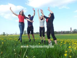 Vier Personen springen fröhlich auf einer blühenden Wiese.