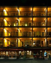 Beleuchtetes Hotelgebäude bei Nacht, mit offenen Balkonen auf mehreren Etagen.