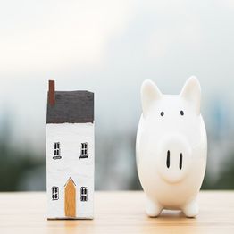 Model house and piggy bank on a table, symbolizing saving for home ownership.
