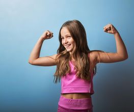 Niña en ropa deportiva rosa sonríe mostrando sus músculos contra un fondo azul.