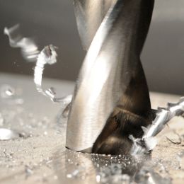 Close-up of a drill bit cutting into metal, surrounded by spirals of metal shavings.