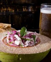Ceviche en coco con cilantro, acompañado de tostadas y cerveza en una jarra.