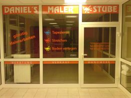 Schaufenster von "Daniel's Malerstube" mit Angeboten wie Tapezieren und Streichen.