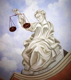 Statua di Giustizia con bilancia in mano, fondo cielo nuvoloso.