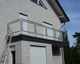 Backsteinfassade mit Balkon und Metallgeländer, Leiter lehnt an der Hauswand.