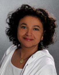 Eine Frau mit lockigem Haar lächelt vor einem grauen Hintergrund.