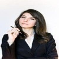 Professional woman in a suit holding a pen, looking thoughtful against a plain background.