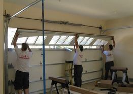 Three people installing a garage door with windows in a spacious garage.