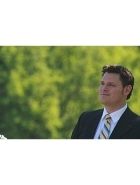 Ein Mann im Anzug blickt nachdenklich zur Seite, Hintergrund ist verschwommenes Grün.