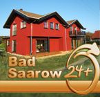 Rotes Haus mit Schriftzug "Bad Saarow 24+" im Vordergrund.