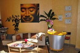Wartezimmer mit Sofa, Pflanzen und Kunstwerk an der Wand, moderner Empfangstresen im Vordergrund.