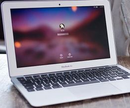 Open MacBook Air displaying login screen on a wooden table.