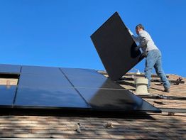 Persoon installeert zonnepanelen op een dak onder een heldere blauwe lucht.