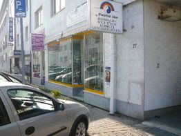 Straßenszene mit geparktem Auto vor einem Laden mit Schildern und Glasfassade.