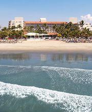 Playa tranquila con palmeras y edificios al fondo bajo un cielo despejado.