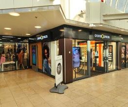 Winkelcentrum met glazen gevel en kledingwinkel links, verlichte ingang en posters in etalage.