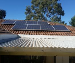 Paneles solares en un techo de tejas bajo un cielo azul, rodeados de árboles.
