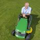 Man smiling while sitting on a green lawn mower on a sunny day.