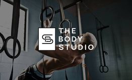 Man traint met ringen in de sportschool, logo 'The Body Studio' op de voorgrond.