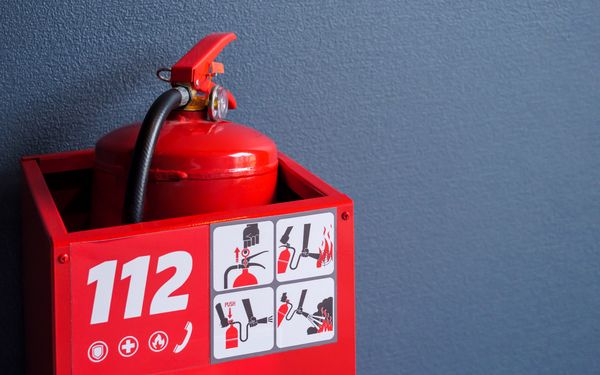 Roter Feuerlöscher in einem Roten Behälter, beschriftet mit 112 als Brandschutzmaßnahmen im Notfall.