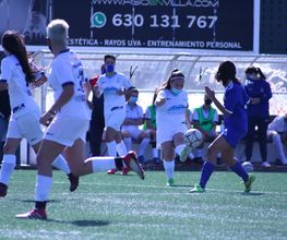 Partido de fútbol femenino, jugadora con balón en primer plano, otras corren en el campo.