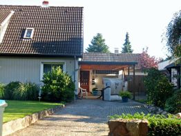Einfamilienhaus mit Garten, Terrasse und überdachtem Eingang, umgeben von Bäumen und Büschen.