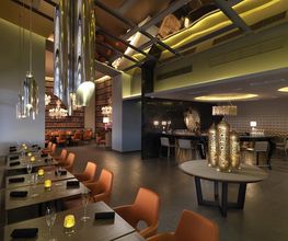 Restaurante moderno con sillas anaranjadas, luces colgantes y mesa decorativa en el centro.