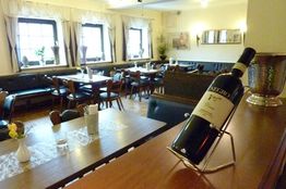 Gemütliches Restaurant mit Holztischen, Stühlen und einer Weinflasche im Vordergrund auf einem Ständer.