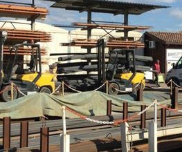Carrelli elevatori gialli in un cantiere con materiali edili e coperture.