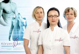 Drei Frauen in weißen Kitteln mit "KörperWelt" Logo, Poster im Hintergrund.
