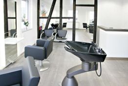 Moderner Friseursalon mit schwarz-weißen Möbeln und Waschbecken auf Holzfußboden.