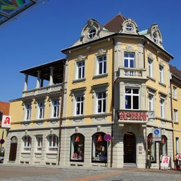 Gelbes historisches Gebäude mit Apotheke im Erdgeschoss, blauer Himmel im Hintergrund.