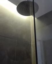 Ducha con cabezal circular y azulejos oscuros, iluminada cálidamente desde arriba.