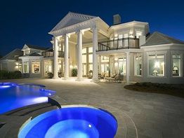 Villa lussuosa di notte con grandi colonne e piscina illuminata, cielo sereno sullo sfondo.