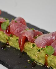 Plato de atún rojo sobre aguacate con sésamo y aderezo en bandeja oscura.