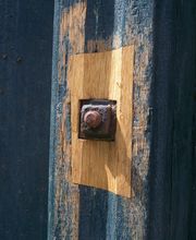 Rostige Metallmutter auf blauem Holz mit freigelegtem hellem Bereich umgeben.