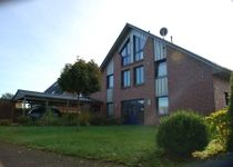 Backsteinhaus mit Garten, großer Fensterfront und Carport an sonnigem Tag.