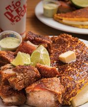 Plato de chicharrón con arepa, acompañado de limón y salsa verde. Bebida Tío Paleta al fondo.
