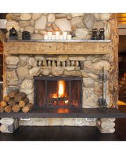 Chimenea de piedra encendida en una sala rústica con leña apilada al lado.