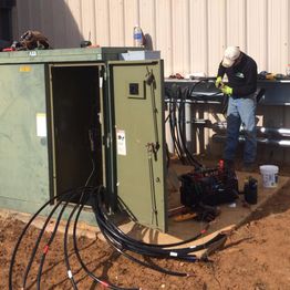 Person working with cables and an electrical box outside a building.