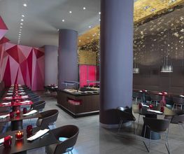 Restaurante moderno con mesas negras, sillas oscuras y decoración geométrica en tonos rojos y dorados.