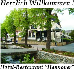 Hotel-Restaurant mit Bäumen am Straßenrand, Beschilderung "Herzlichen Willkommen!" und "Hannover".