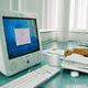 Alter Mac-Computer auf Schreibtisch mit Tastatur und Papier, Person blättert durch Unterlagen.