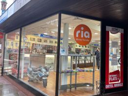 Schaufenster eines Ladens mit Ria-Geldtransfer und Ortel Mobile Werbung, Spielzeug-Motorrad innen.