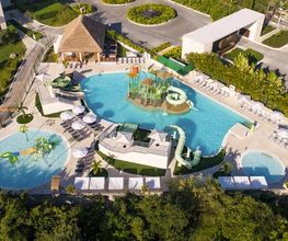Vista aérea de un resort con múltiples piscinas y áreas de descanso cerca de un edificio moderno.