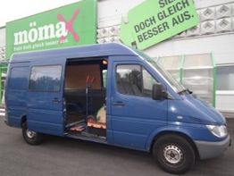 Blauer Lieferwagen mit offener Schiebetür vor einem Möbelgeschäft.