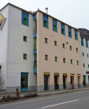 Mehrfarbiges Gebäude mit Schildern und Fenstern an einer Straße, Berge im Hintergrund.