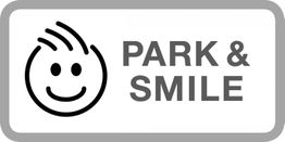 Weiße Tafel mit Smiley und der Aufschrift "Park & Smile" in grauer Schrift.
