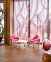 Dos sillas rosas y una mesa blanca frente a cortinas altas y onduladas en un salón elegante.